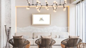 Un salon moderne avec un canapé blanc, trois fauteuils en osier, un logo encadré accroché au mur et un luminaire original.