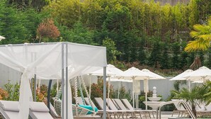 Un espace piscine aménagé avec des chaises longues, des parasols et un abri de type cabane.