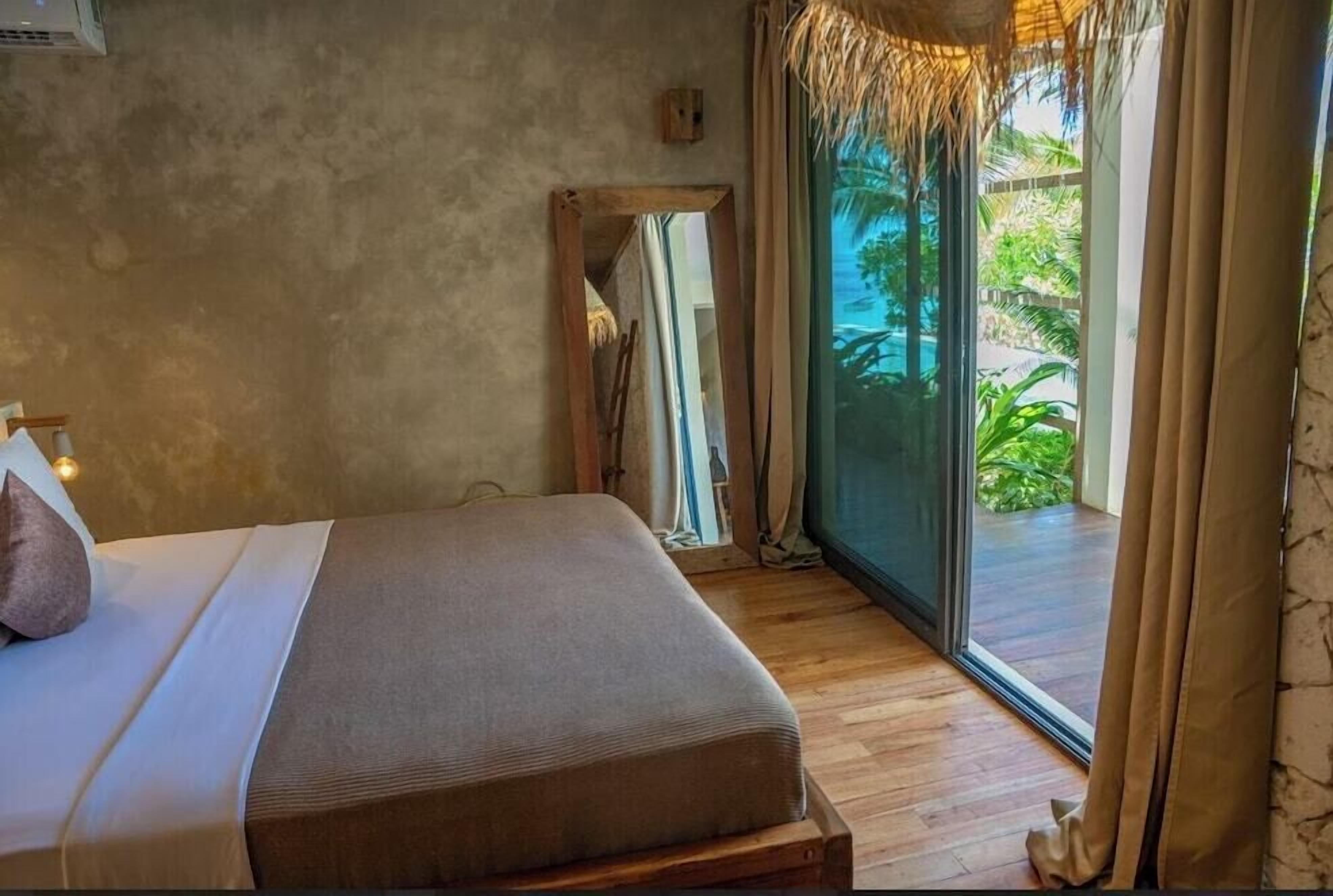 A bedroom with a bed, a mirror, and a view of greenery through a glass door.