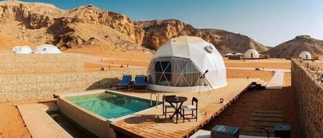 A desert resort with a swimming pool, outdoor seating, and dome-shaped accommodations.
