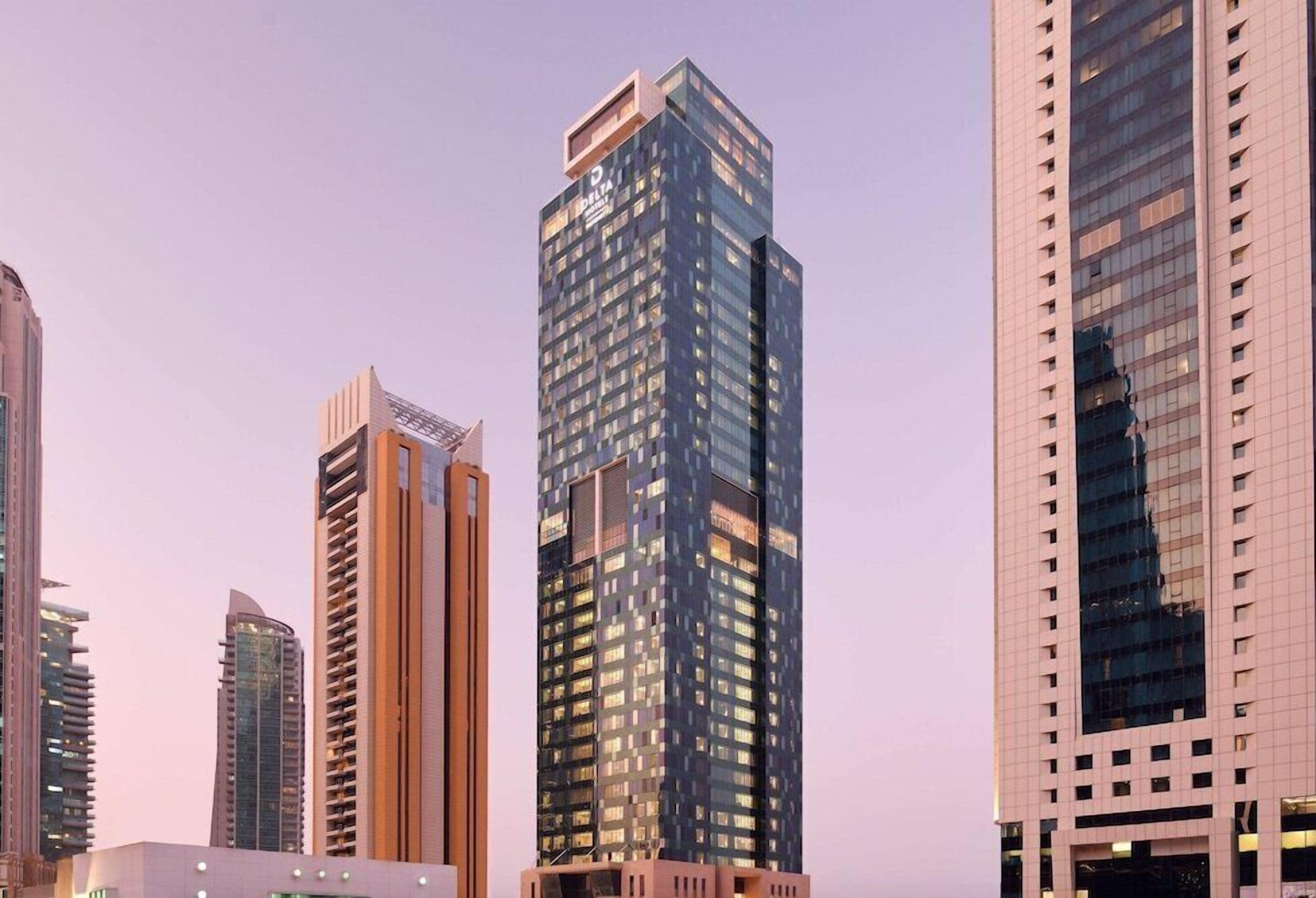 A high-rise building with a modern glass facade, multiple floors, and a prominent logo at the top.