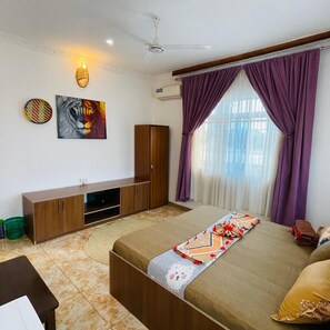 A bedroom with a bed, a TV stand, a wardrobe, and a window with purple curtains. - Max Hotel Nungwi (Nungwi)