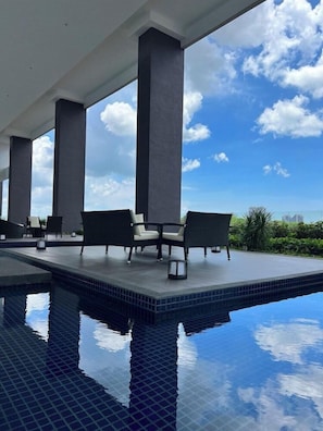 An infinity pool with a clear view of the sky and greenery, surrounded by dark-toned lounge chairs and a tiled deck. - Courtyard Melaka (Malacca City)
