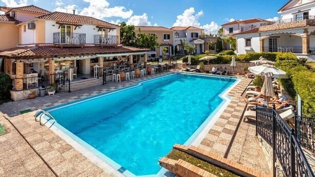Une piscine entourée d’un patio aménagé avec des espaces de détente en plein air et un bar.