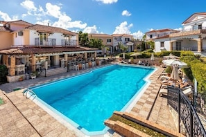 Una piscina rodeada de un patio con mobiliario exterior y un bar.
