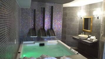 Un baño moderno con una bañera grande, un lavamanos pequeño y un espejo.