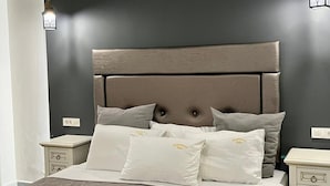 Un lit bien fait, avec une tête de lit matelassée, des oreillers blancs et une serviette blanche roulée posée sur le lit.