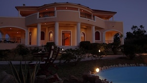 Une grande maison à deux étages, dotée d’une piscine, de colonnes et d’un patio couvert.
