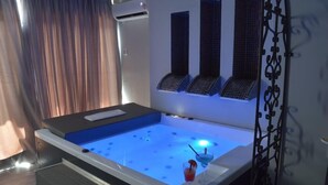 Un bain à remous moderne, avec un éclairage bleu à l’intérieur, une petite table avec une boisson et une porte décorative en métal.