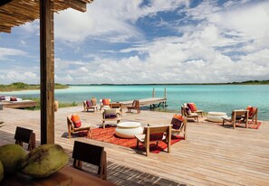 A wooden deck with lounge chairs and ottomans, overlooking a turquoise sea. - Our Habitas Bacalar (Bacalar)