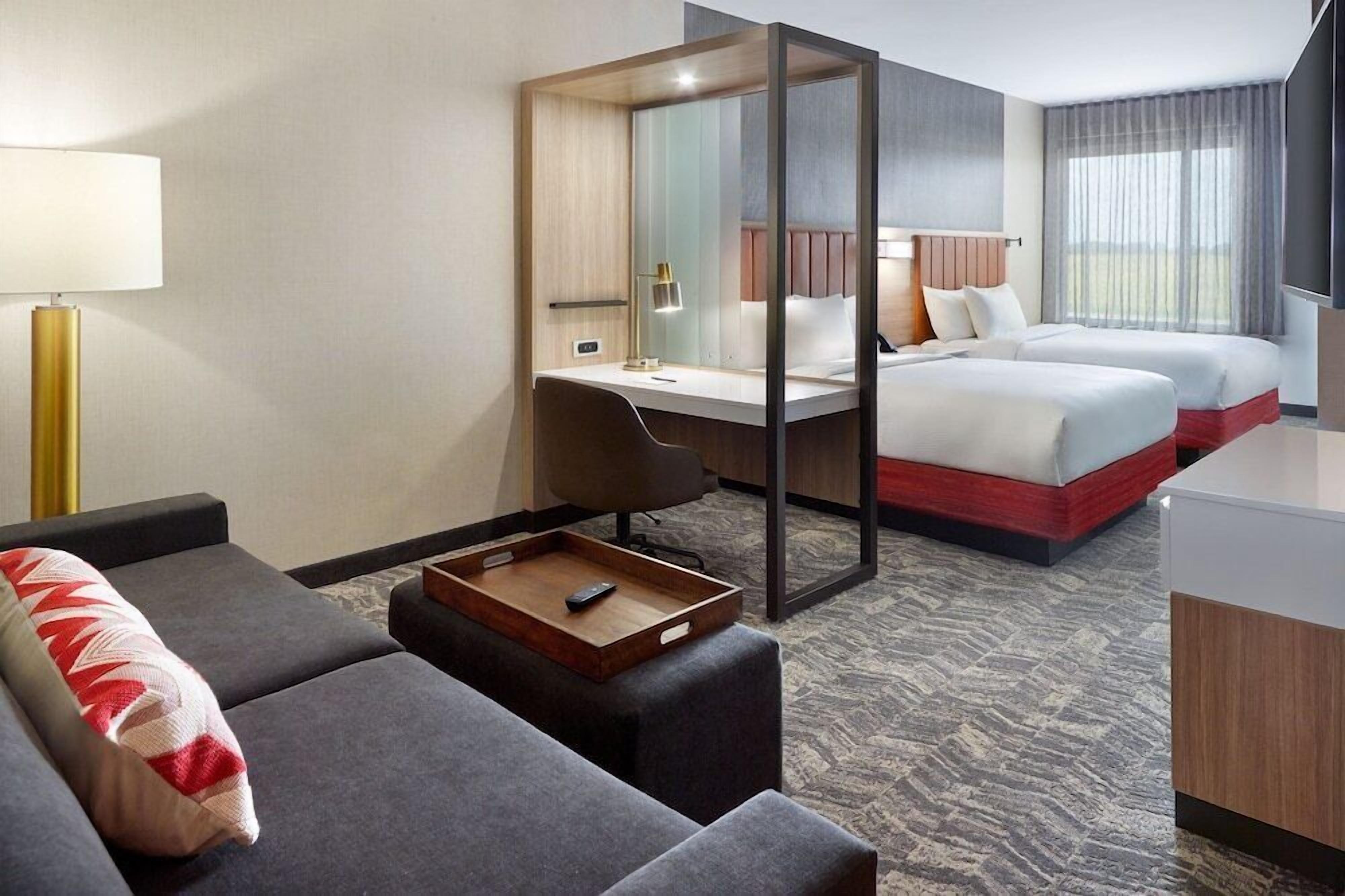 A hotel room with a desk, two beds, a sofa, a tray table, and a large window.