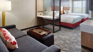 Quarto de hotel com escrivaninha, duas camas, um sofá, uma mesinha de apoio e uma janela grande.