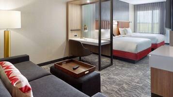 A hotel room with a desk, two beds, a sofa, a tray table, and a large window.