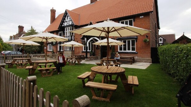 A traditional pub with outdoor seating, including wooden tables and benches, and umbrellas providing shade. - The Bears Paw Inn (Sandbach)