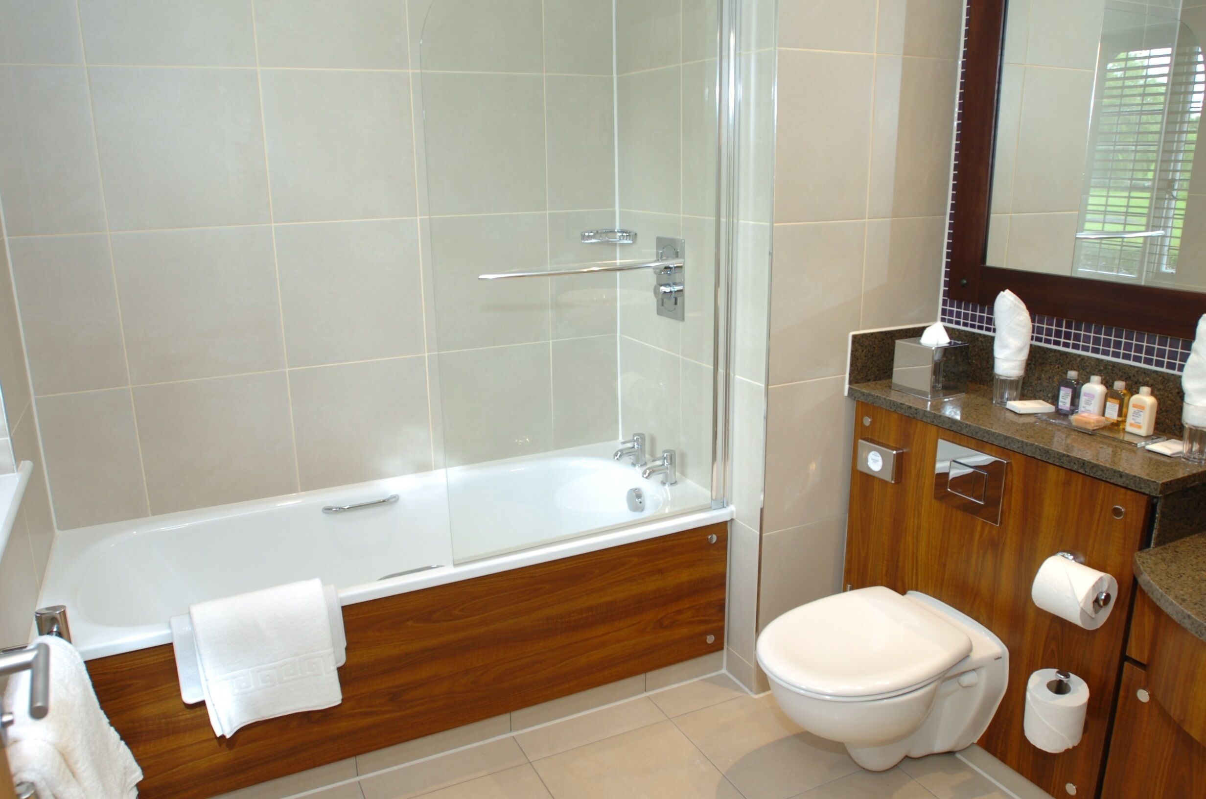 A modern bathroom with a glass-enclosed shower, a wooden vanity, a toilet, and a large mirror.