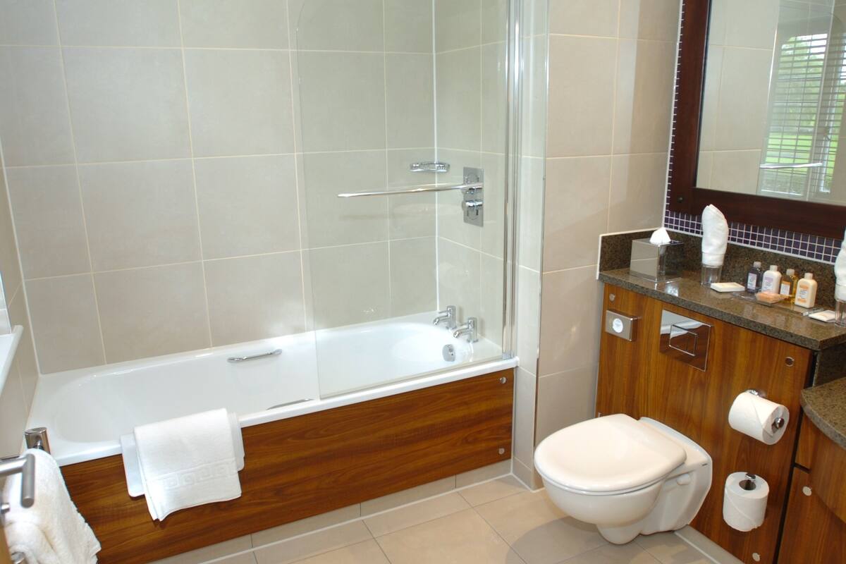 A modern bathroom with a glass-enclosed shower, a wooden vanity, a toilet, and a large mirror.