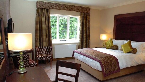 Een hotelkamer met een bed, twee bedlampen, een stoel, een bureau en een raam met gordijnen.