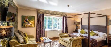 A four-poster bed with a wooden headboard, a sofa, a chair, and a small table in a well-lit room with a large window.