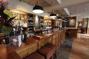 A bar area with wooden counters, hanging pendant lights, and a menu board. - The Bears Paw Inn (Sandbach)