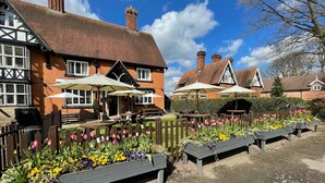 A traditional building with a tiled roof, wooden benches, and flower beds. - The Bears Paw Inn (Sandbach)