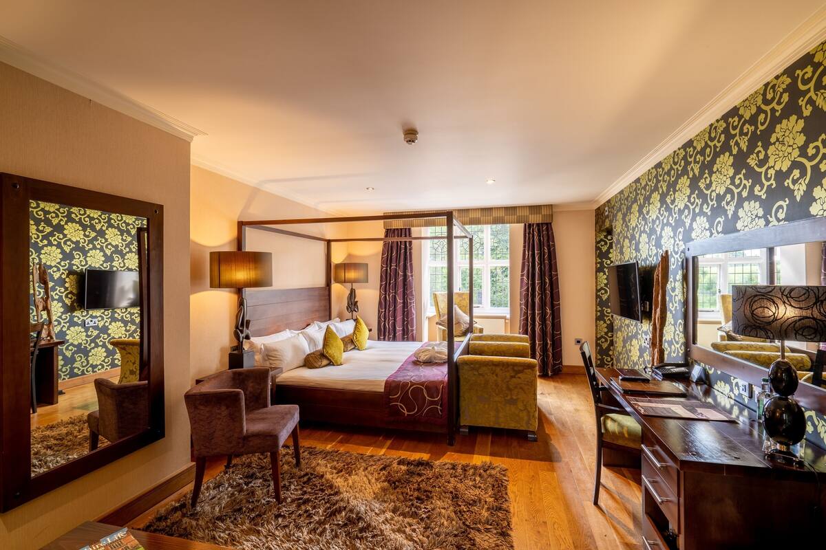A bedroom with a large bed, a desk, a chair, a mirror, and a window with curtains.