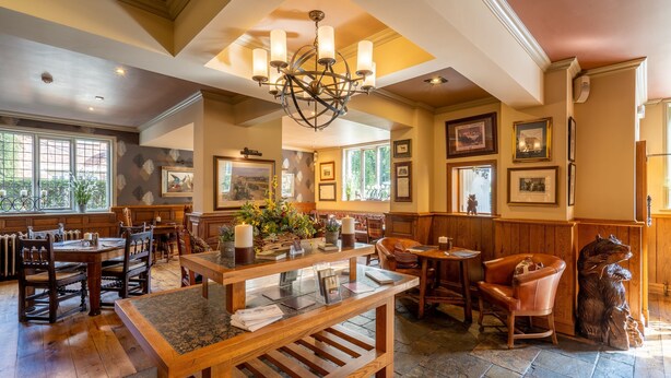 A spacious dining area with wooden tables and chairs, a central island with a marble top, and a chandelier. - The Bears Paw Inn (Sandbach)