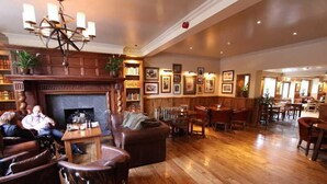 A spacious lobby with a fireplace, wooden flooring, leather seating, and a dining area. - The Bears Paw Inn (Sandbach)