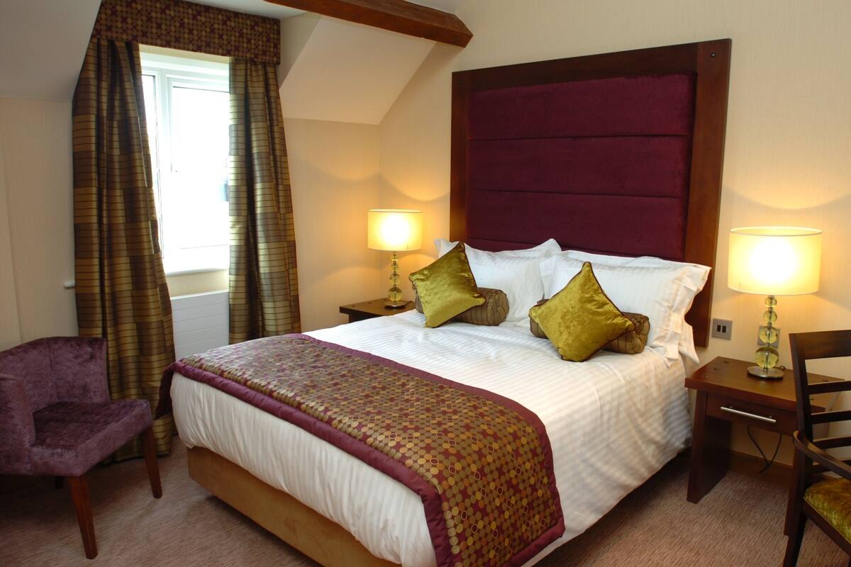 A hotel room with a large bed, two bedside lamps, a chair, and a window with curtains.