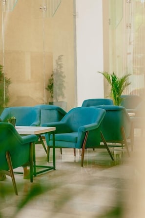 A modern indoor seating area with blue chairs and a small table, surrounded by glass walls and plants. - The Fern - An Ecotel Hotel, Alwar (Alwar)