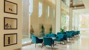 A spacious lobby with teal chairs and tables, large windows, and framed artwork on the walls. - The Fern - An Ecotel Hotel, Alwar (Alwar)