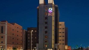 A multi-story hotel with a prominent logo on the facade, featuring a modern architectural design with a mix of glass and concrete materials.