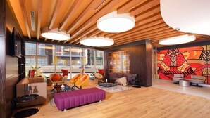 A modern hotel lobby with wooden ceiling beams, large windows, and a vibrant abstract mural.