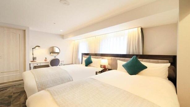 Een hotelkamer met twee bedden, een bureau met lamp, een spiegel en een raam met gordijnen.