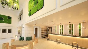 Een ruime lobby met een centraal zitgedeelte, een receptiebalie en een groene wand.