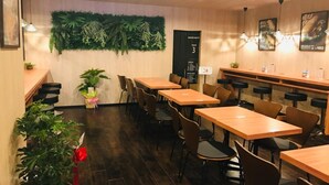 A restaurant interior with wooden tables and chairs, a green wall with plants, and a menu board. - Hotel Live Max Nagoya Sakuradoriguchi (Nagoya)