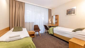 A hotel room with two beds, a desk, a chair, and a large window with curtains.