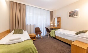 Une chambre d’hôtel avec deux lits, un bureau, une chaise et une grande fenêtre avec des rideaux.