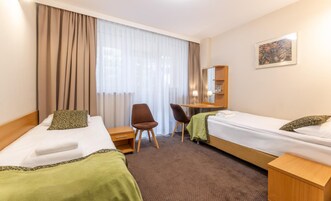 Habitación de hotel con dos camas, un escritorio, una silla y un amplio ventanal con cortinas.
