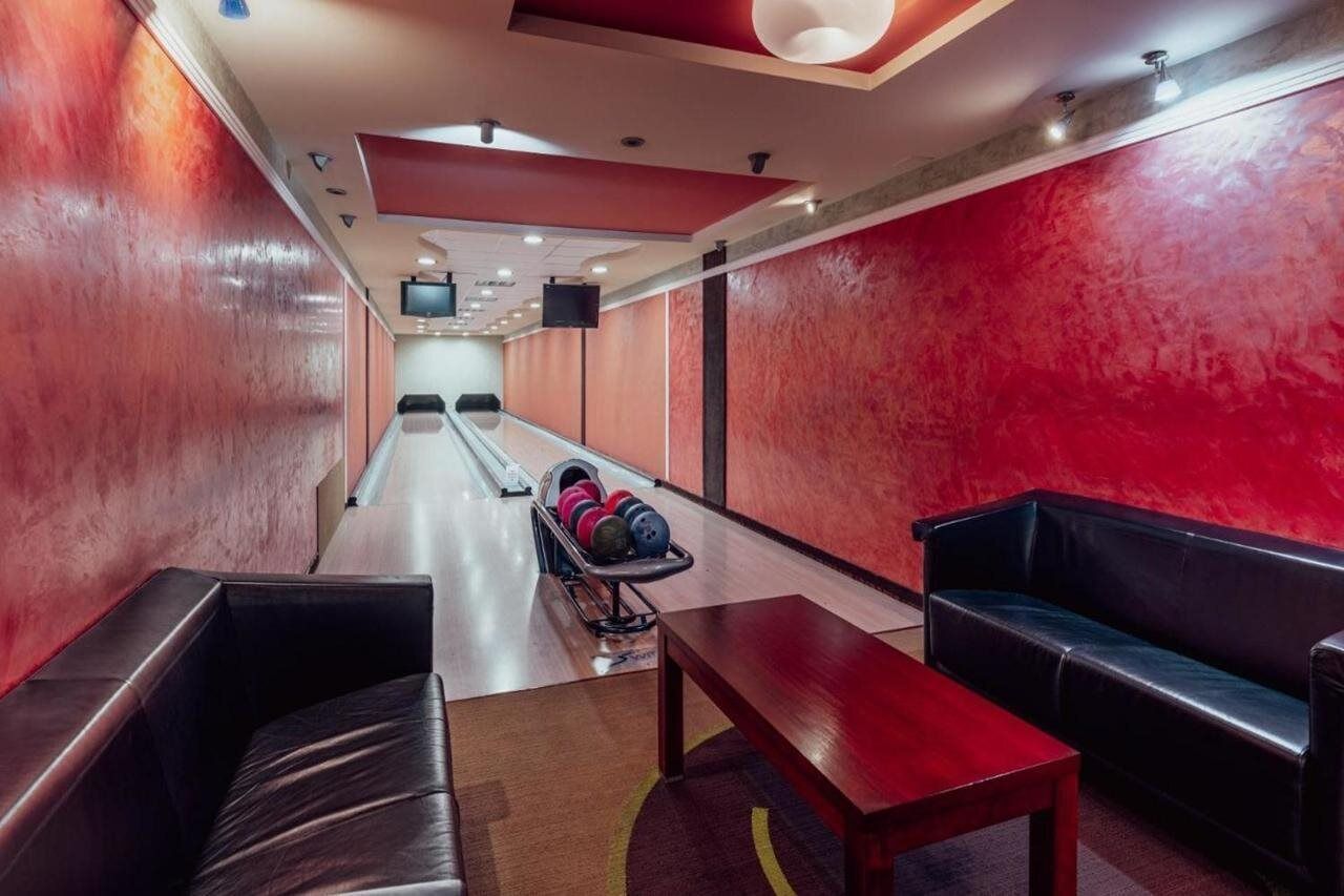 Een bowlingbaan met een rode muur, een houten vloer en een zwarte leren bank.