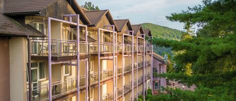 Un hotel de varios pisos con balcones, un camino de ladrillo y follaje circundante.