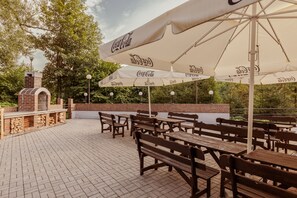 Un patio exterior con suelo de ladrillo, bancos y mesas de madera bajo sombrillas con la marca Coca-Cola.