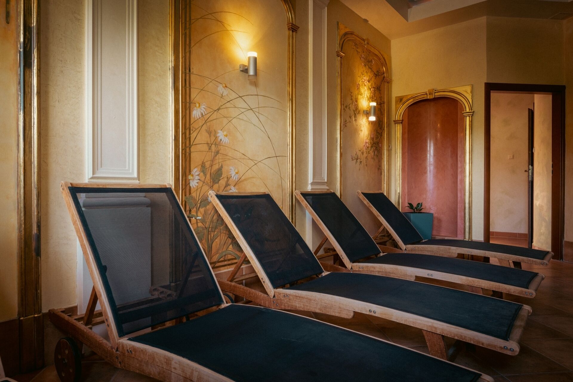 A spa room with wooden sun loungers, a wall-mounted light fixture, and a door with a decorative arch.