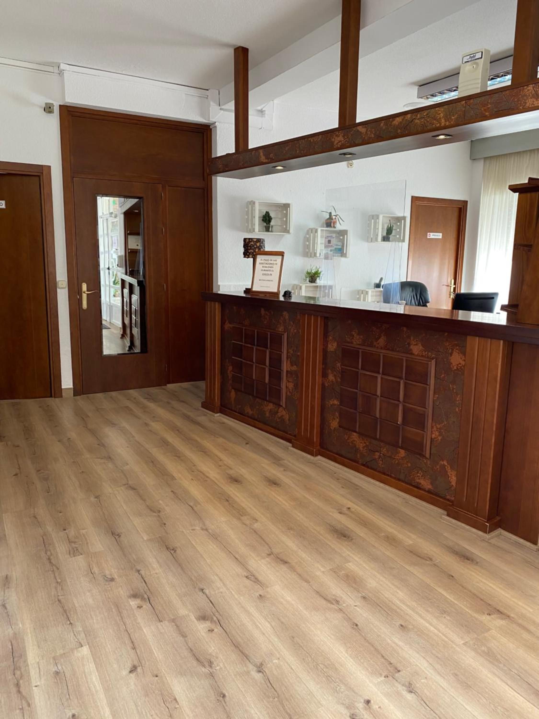 Zona de recepción con un mostrador de madera, un cartel enmarcado, una planta pequeña y una puerta que da a otra habitación.