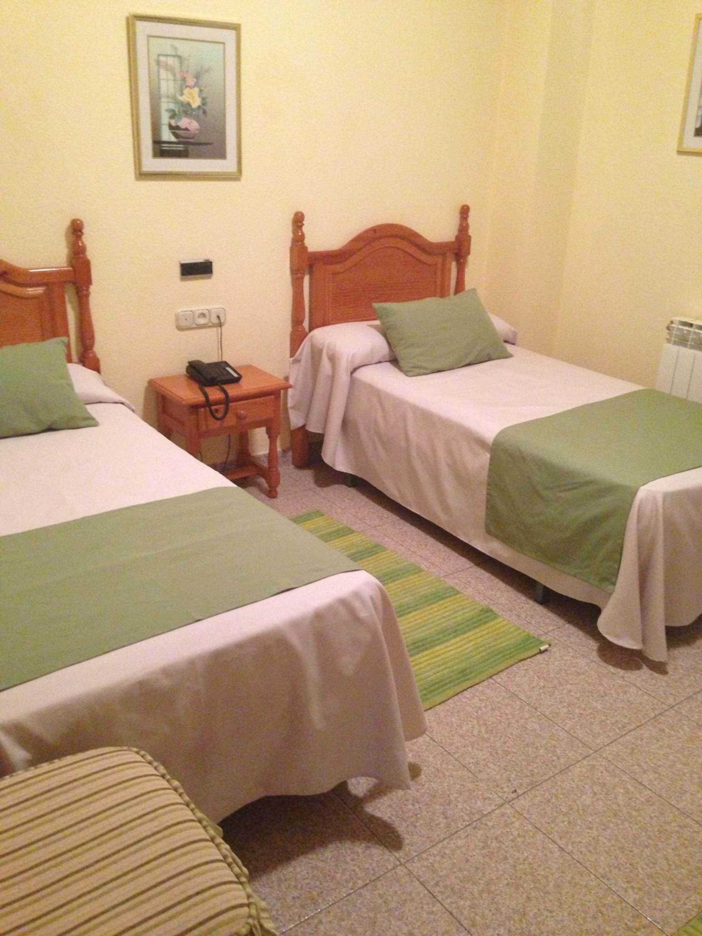 Habitación de hotel con dos camas individuales, una mesita de noche con teléfono, toma de corriente y radiador.
