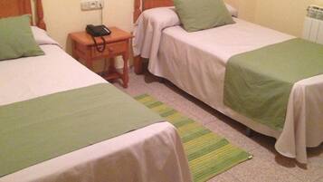 Habitación de hotel con dos camas individuales, una mesita de noche con teléfono, toma de corriente y radiador.