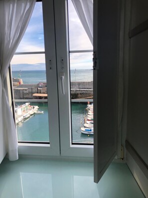 A room with a large window overlooking a marina with boats docked. - Hotel El Puerto (Mundaka)