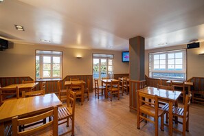 A dining area with wooden tables and benches, large windows, and a flat-screen TV mounted on the wall. - Hotel El Puerto (Mundaka)