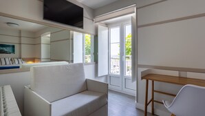 Una sala de estar moderna con un sofá, una mesa de madera, un televisor montado en la pared y un amplio ventanal con vistas al follaje exterior.