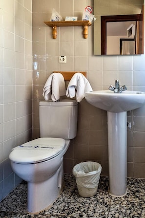 Un baño con inodoro, lavamanos y un cubo de basura.