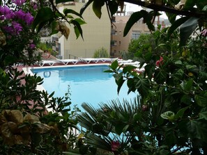 A swimming pool surrounded by lush greenery and white lounge chairs. - Hotel Jardin (Oropesa del Mar)
